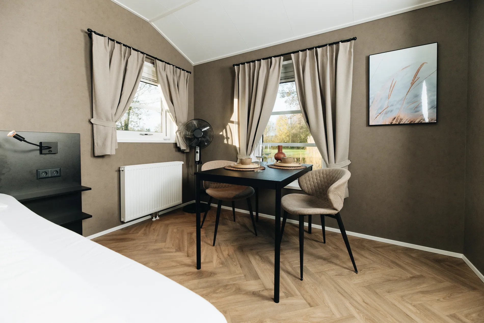 Interieur van een luxe lodge bij Resort Land & Zee met een moderne zwarte eethoek, visgraatvloer, stijlvolle wanddecoratie en uitzicht op de omliggende natuur.